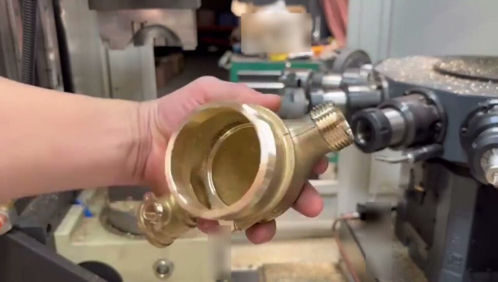 Finished brass multi-port valve body shown after machining in front of the machine setup